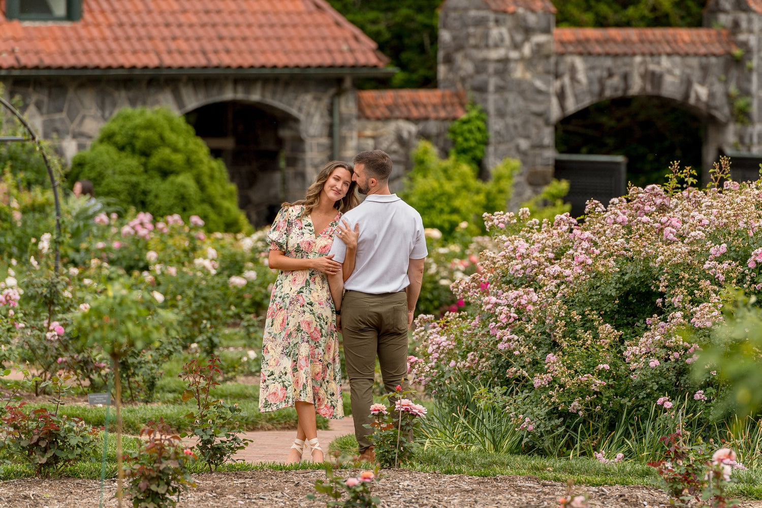 Couple walking through a garden with stone buildings in the background